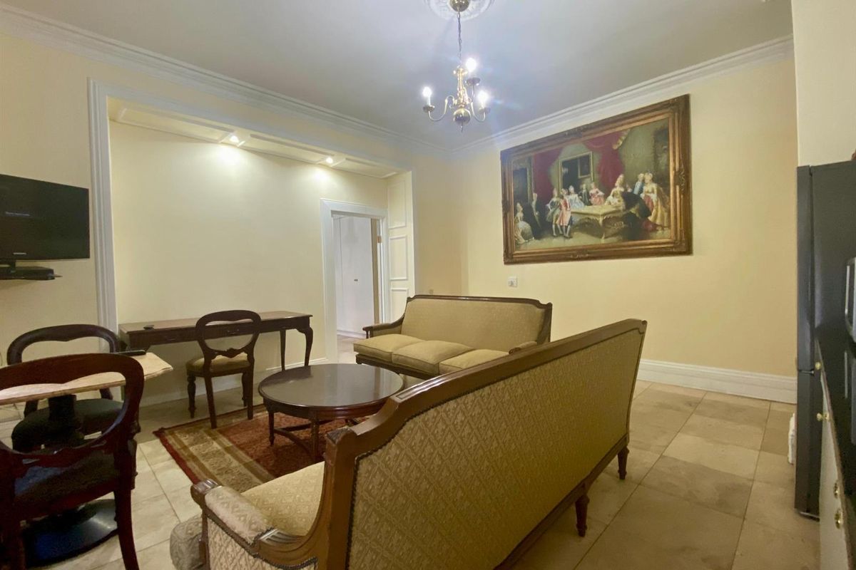 A spacious living area featuring tiled flooring, decorative ceiling rose, and recessed lighting, providing a comfortable and classic living space.