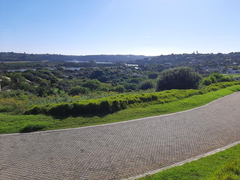 A scenic view overlooking a lush green landscape and residential area, featuring a paved driveway in the foreground.