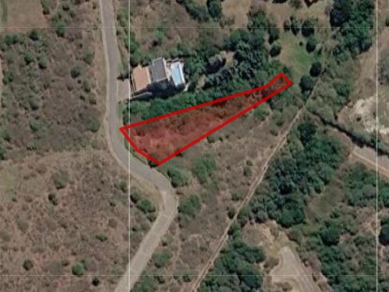 Aerial view of a vacant residential plot highlighted in red, showing its shape and proximity to local road infrastructure and surrounding vegetation.