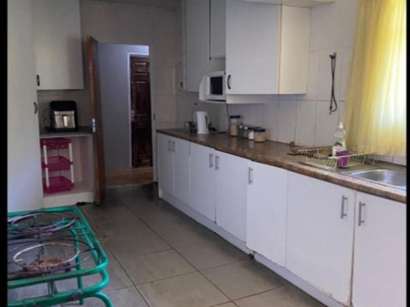 A functional kitchen featuring white cabinetry, laminate countertops, and tiled flooring. The space offers a practical layout with integrated sink and storage.