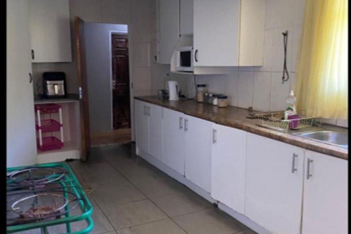 A functional kitchen featuring white cabinetry, laminate countertops, and tiled flooring. The space offers a practical layout with integrated sink and storage.