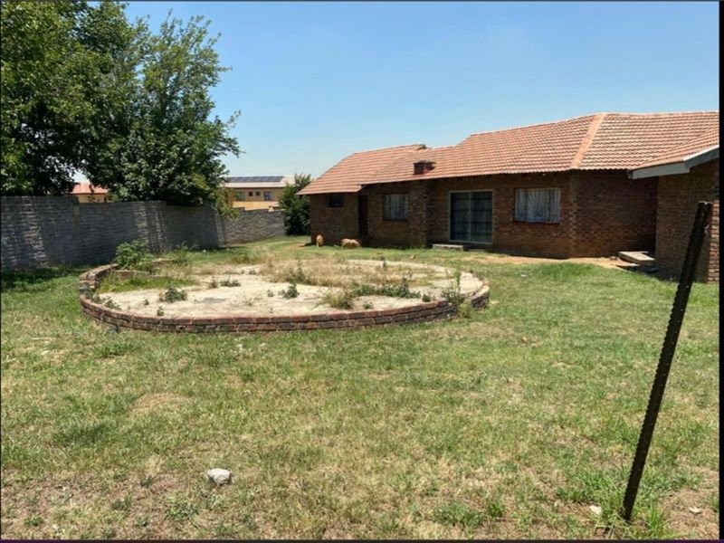Rear view of a brick house featuring a large garden with a circular brick planter and perimeter walling, requiring landscaping and exterior maintenance.