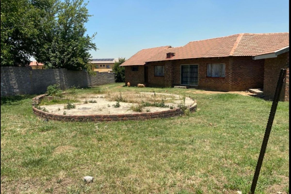 Rear view of a brick house featuring a large garden with a circular brick planter and perimeter walling, requiring landscaping and exterior maintenance.