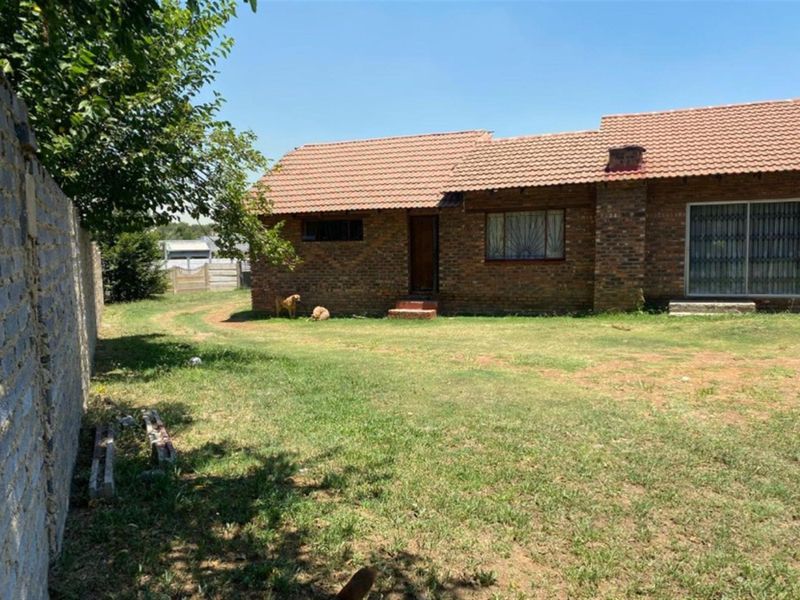Rear view of a single-story brick house featuring a tiled roof, sliding glass doors with security gates, and a large backyard area.