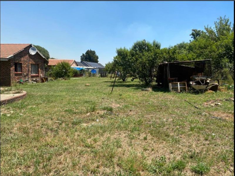 A spacious backyard featuring a large lawn area, mature trees, and a brick-built house with a tiled roof.