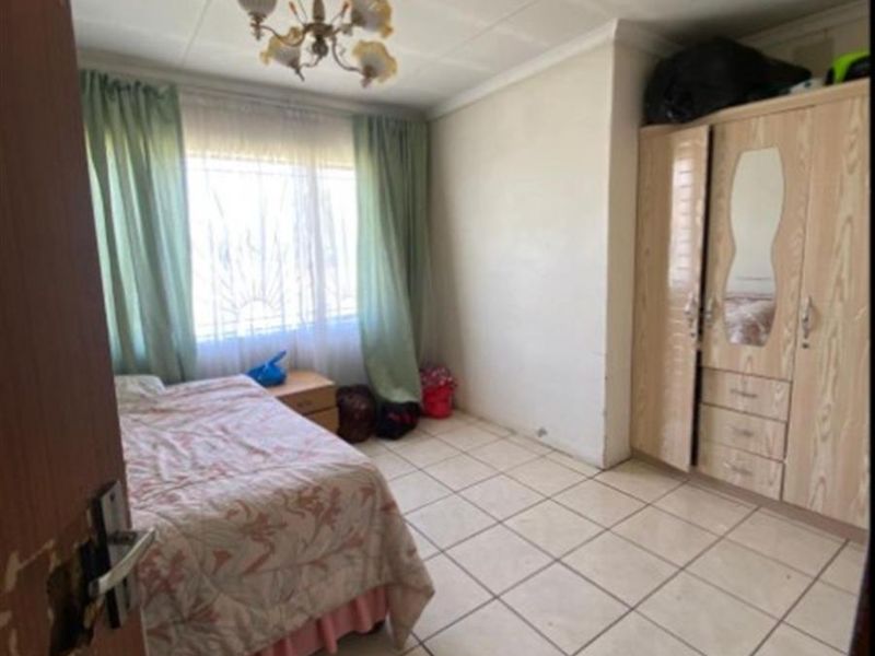A bedroom featuring tiled flooring, a built-in wardrobe, and security bars on the window. The room requires minor repairs to the door and ceiling.