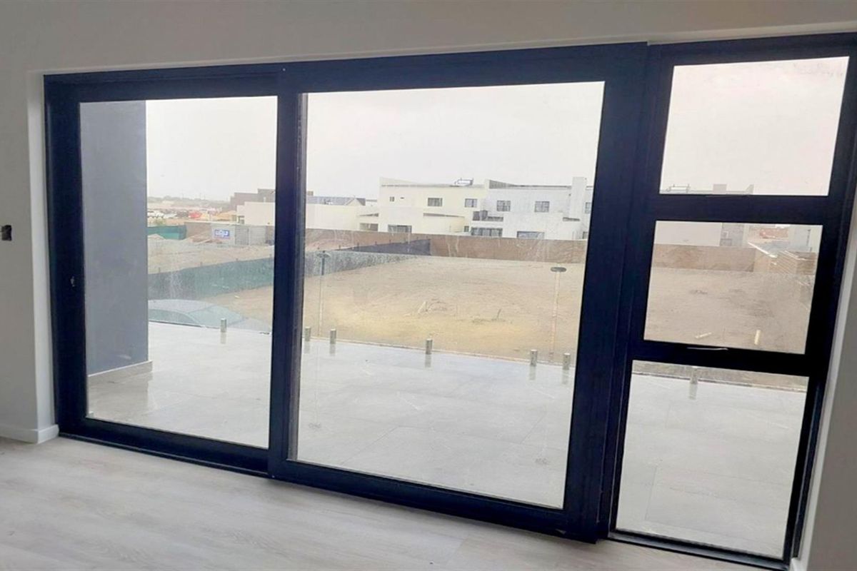 Bright living area featuring large sliding glass doors that open onto a tiled balcony with a glass balustrade, offering an unobstructed view.