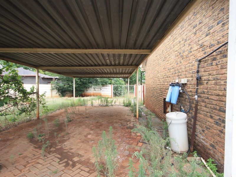A covered carport area featuring brick paving and an external water filtration system mounted to the side brick wall.