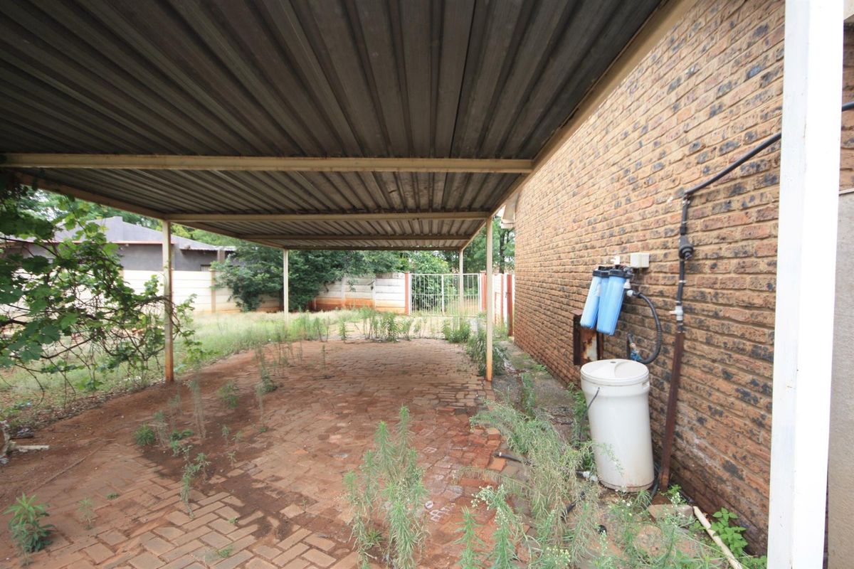 A covered carport area featuring brick paving and an external water filtration system mounted to the side brick wall.