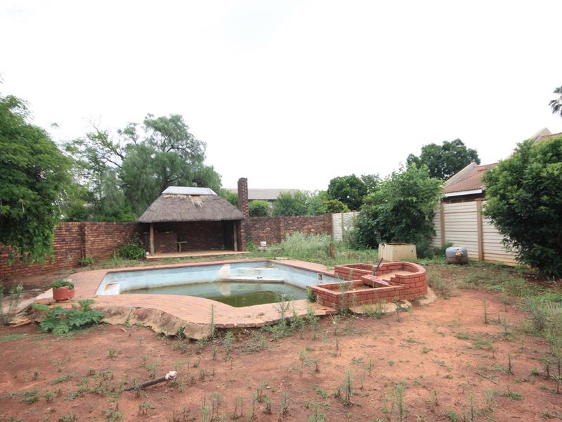 Outdoor pool area featuring a swimming pool, brick paving, and a thatched lapa, currently requiring significant landscaping and pool maintenance.
