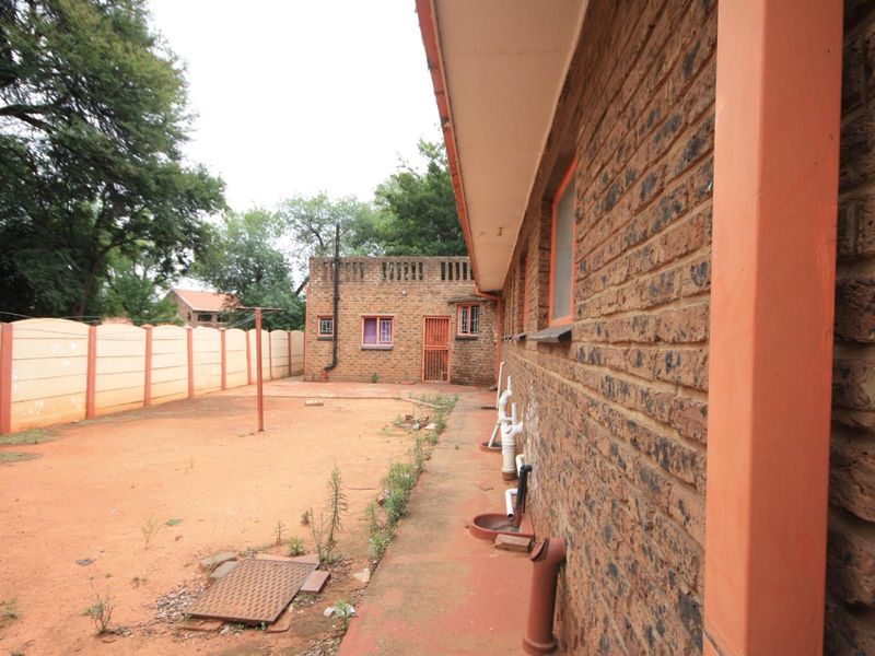 Rear exterior view of the property featuring a face brick facade, concrete pathway, and a large, unlandscaped backyard enclosed by precast boundary walls.