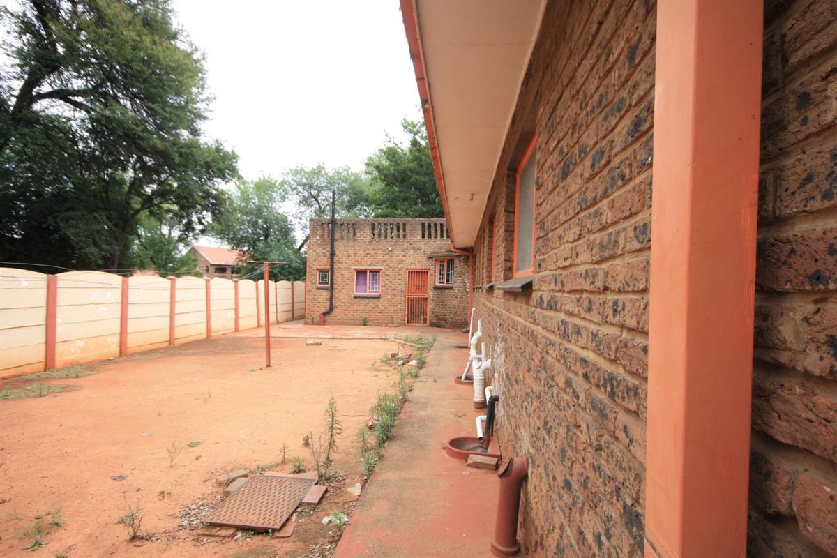 Rear exterior view of the property featuring a face brick facade, concrete pathway, and a large, unlandscaped backyard enclosed by precast boundary walls.