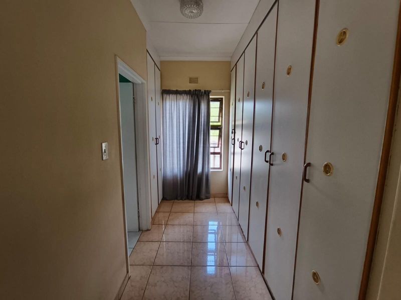 A bright hallway featuring extensive built-in cupboard storage, tiled flooring, and a window allowing natural light.