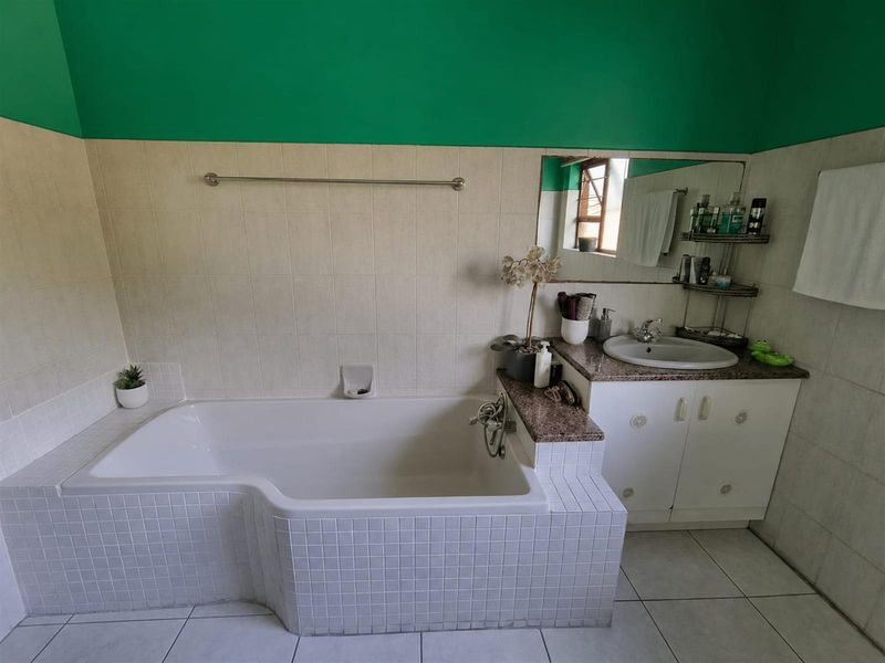 A functional bathroom featuring a built-in tiled bathtub, a vanity cabinet with a granite countertop, and a wall-mounted mirror.