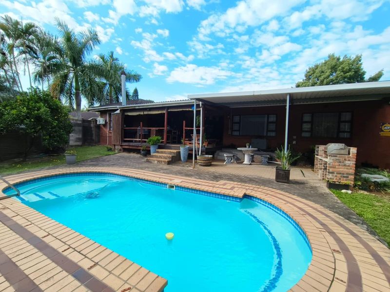 A backyard area featuring a swimming pool, paved surround, and a covered patio with a built-in brick braai.