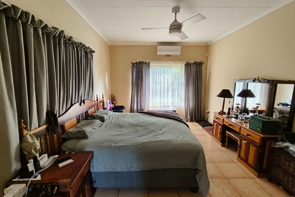 Spacious bedroom featuring tiled flooring, a ceiling fan, and a wall-mounted split-system air conditioner for climate control.