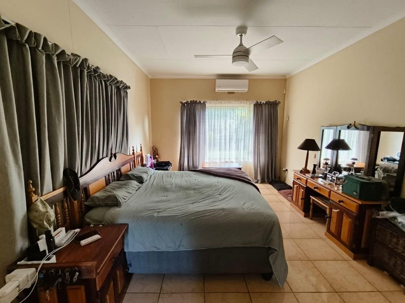 Spacious bedroom featuring tiled flooring, a ceiling fan, and a wall-mounted split-system air conditioner for climate control.