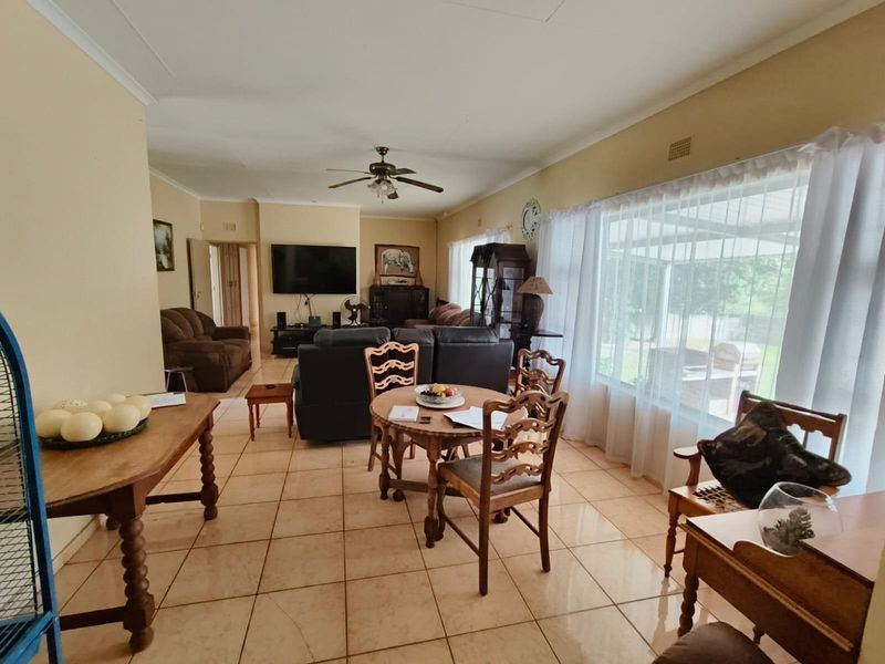 Spacious open-plan living and dining area featuring ceramic tiled flooring, large windows for natural light, and a ceiling fan.