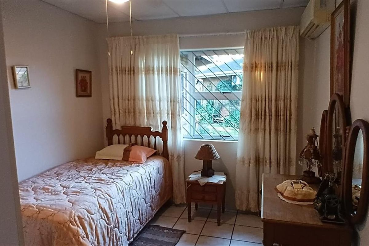 A functional bedroom featuring tiled flooring, a window with security bars, and a wall-mounted air conditioning unit.