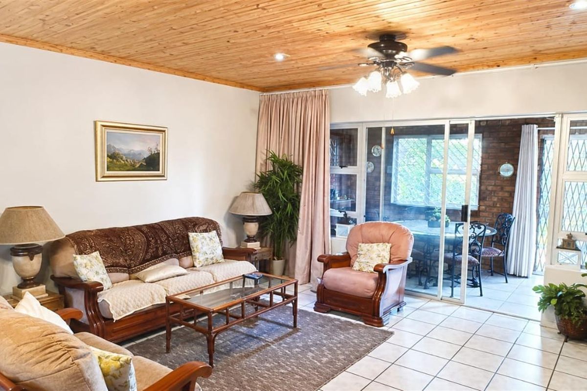 A living room featuring a timber-clad ceiling, tiled flooring, and sliding glass doors that open onto an enclosed patio area.