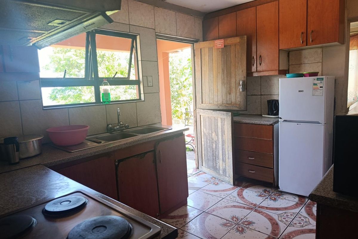 A dated kitchen featuring wooden cabinetry, tiled flooring, a built-in hob, and direct access to an outdoor area.