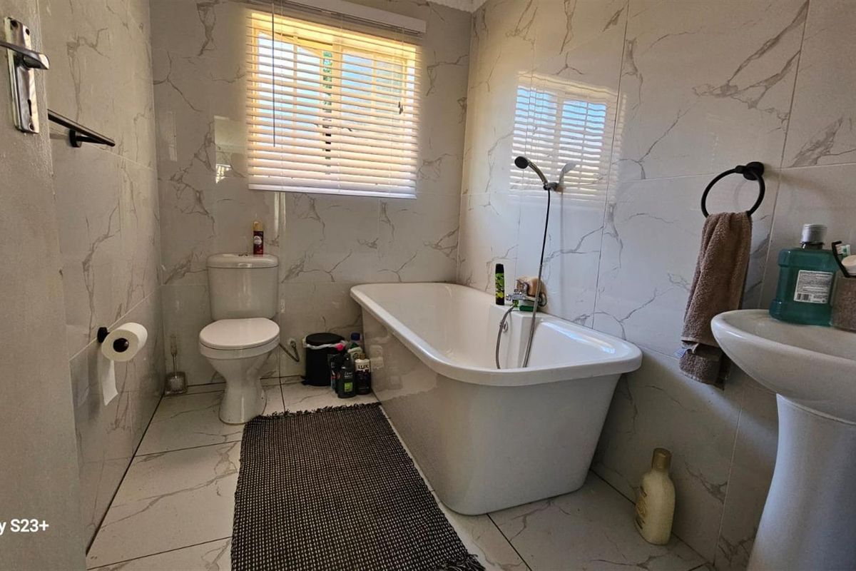 A modern bathroom featuring marble-look wall and floor tiles, a freestanding bathtub with a handheld shower attachment, a pedestal basin, and a toilet.