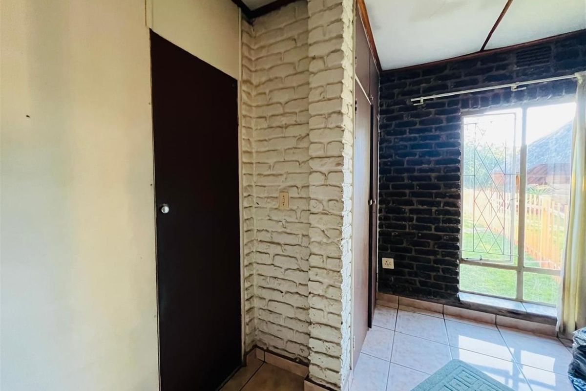 Interior view of a room featuring exposed brickwork, tiled flooring, and a large window providing natural light.