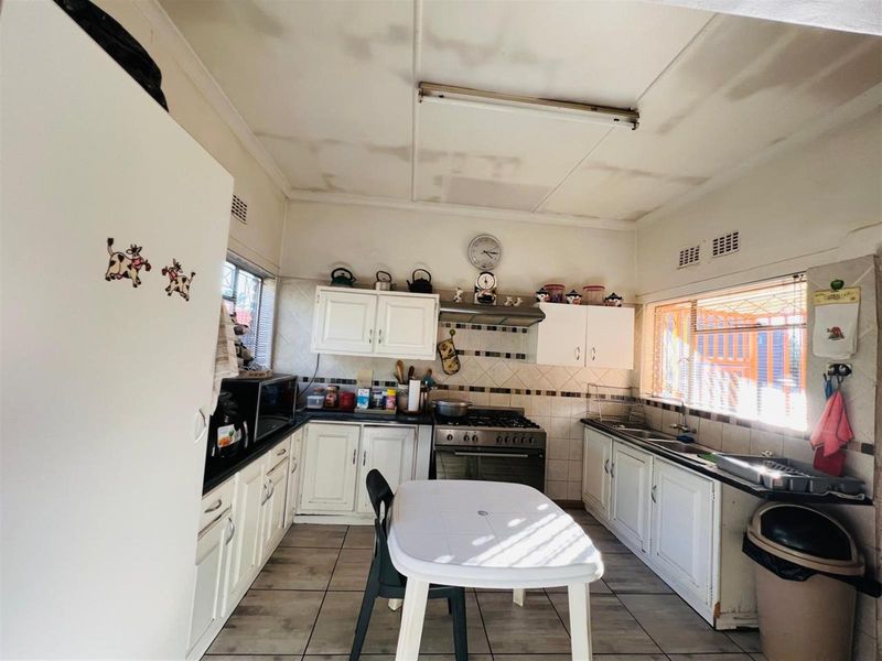 A functional kitchen featuring white cabinetry, a gas stove with extractor fan, tiled flooring, and ample natural light from multiple windows.