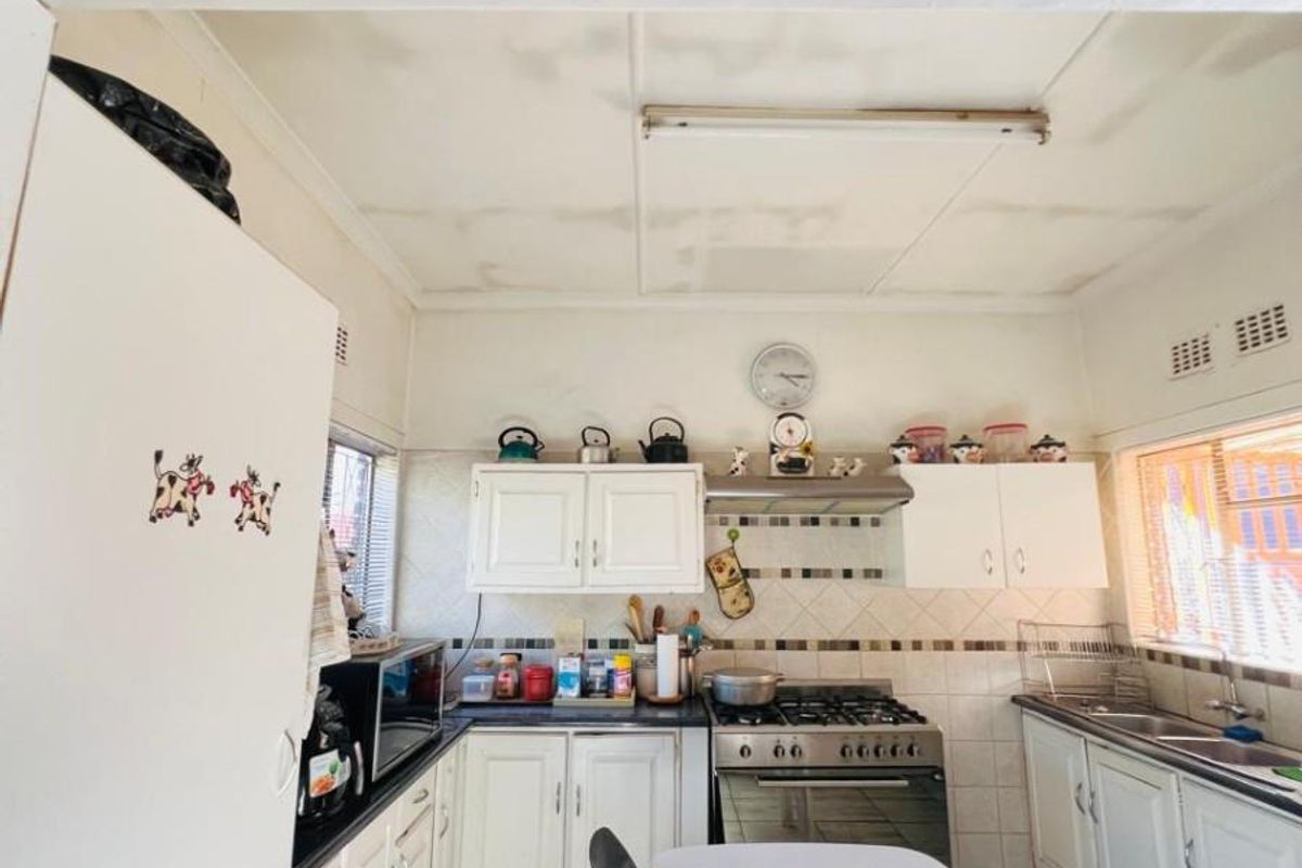 A functional kitchen featuring white cabinetry, a gas stove with extractor fan, tiled splashbacks, and a double sink.
