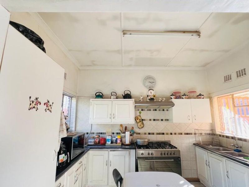 A functional kitchen featuring white cabinetry, a gas stove with extractor fan, tiled splashbacks, and a double sink.