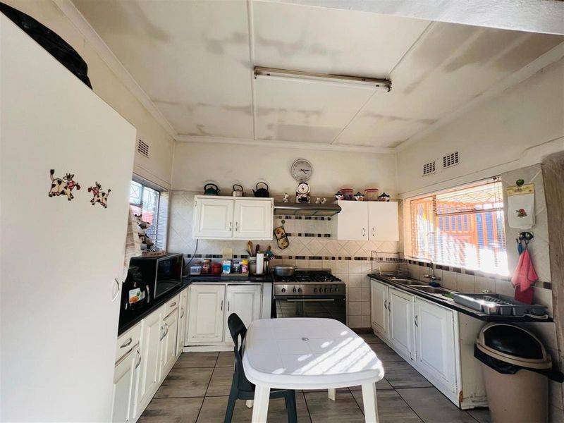 A dated kitchen featuring white cabinetry, tiled backsplash, a gas stove with extractor fan, and tiled flooring.