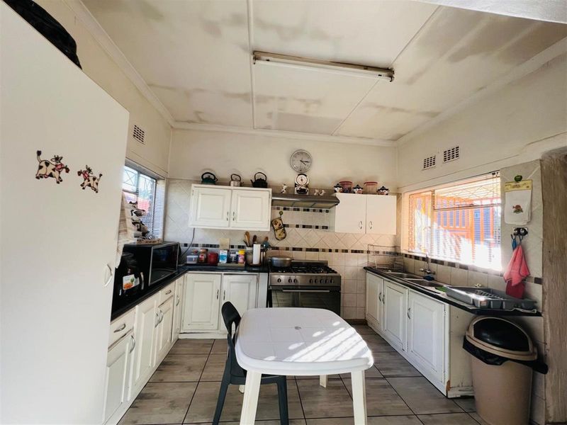 A functional kitchen featuring white cabinetry, tiled countertops, a gas stove with extractor fan, and tiled flooring.