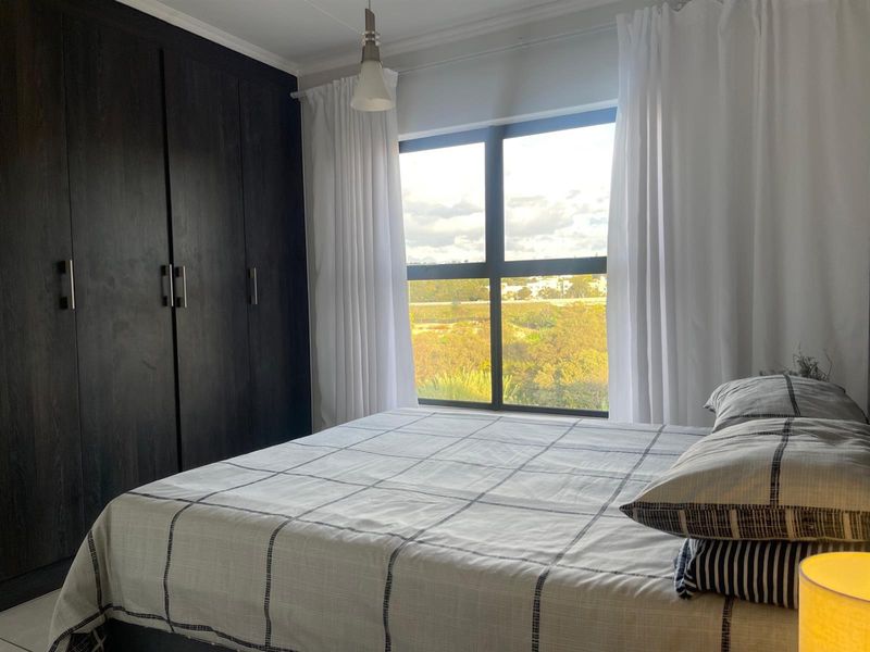 A well-maintained bedroom featuring dark built-in cupboards, a large window with natural light, and a pleasant exterior view.