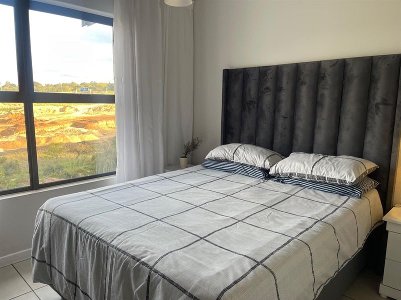 A well-lit bedroom featuring large windows with natural light and tiled flooring, offering a clear view of the surrounding landscape.
