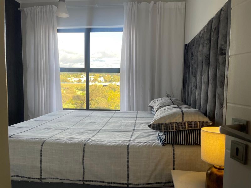 A well-lit bedroom featuring a large window with natural views and a modern upholstered headboard.