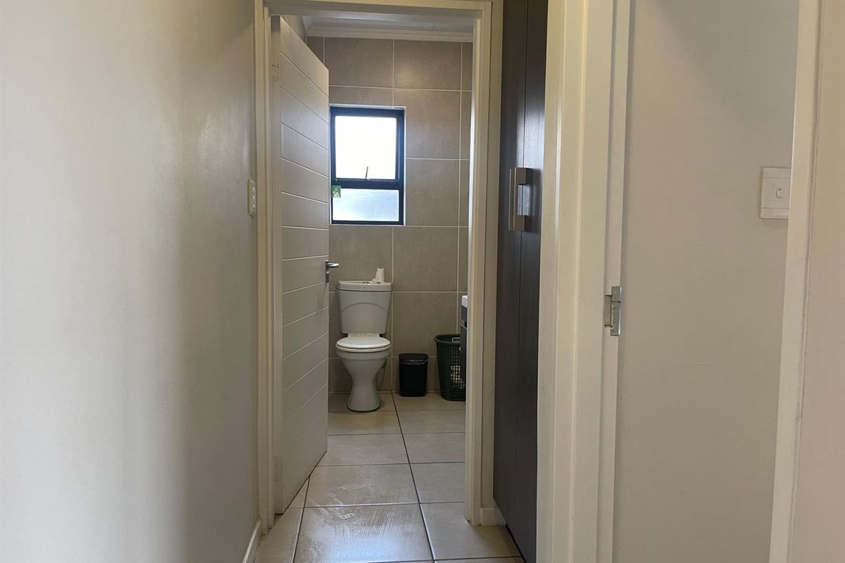 A functional bathroom featuring tiled walls and flooring, a standard toilet, and a built-in storage cupboard, viewed from the adjacent hallway.