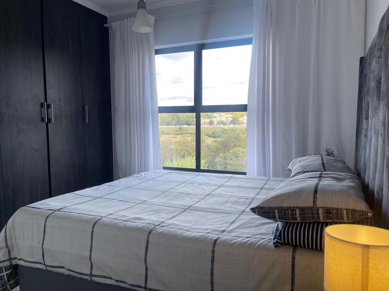 A well-maintained bedroom featuring dark built-in cupboards, a large window with natural light, and a pleasant exterior view.