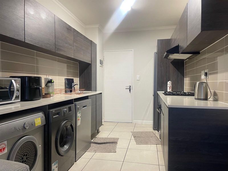 Modern galley-style kitchen featuring dark wood-grain cabinetry, stone countertops, gas hob, extractor fan, and tiled finishes throughout.