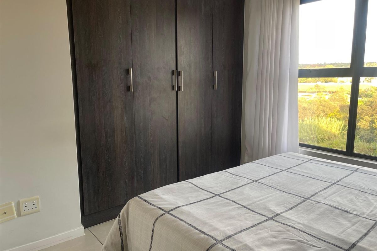 A bright bedroom featuring dark wood built-in cupboards, tiled flooring, and a large window offering natural light and scenic views.