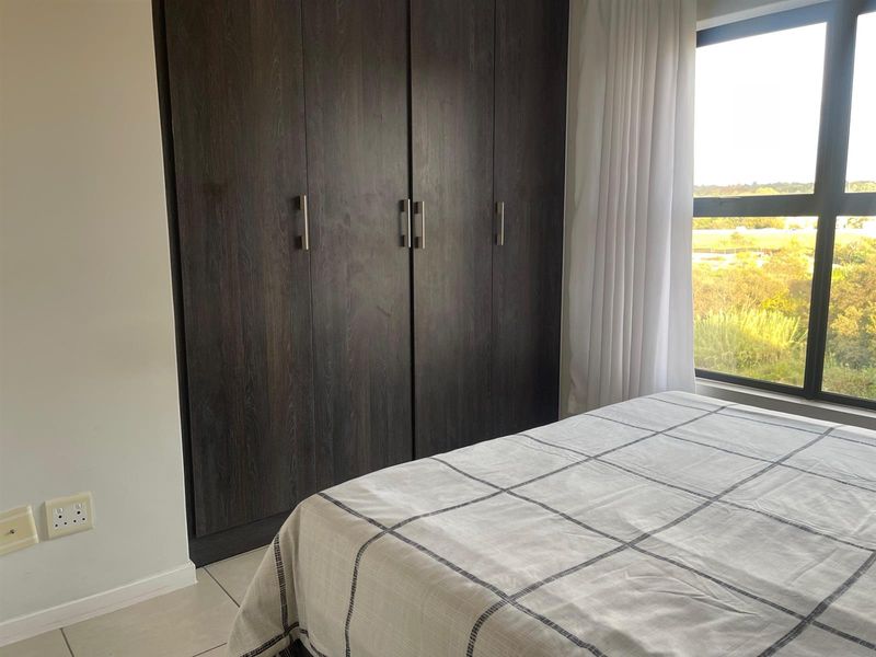 A bright bedroom featuring dark wood built-in cupboards, tiled flooring, and a large window offering natural light and scenic views.