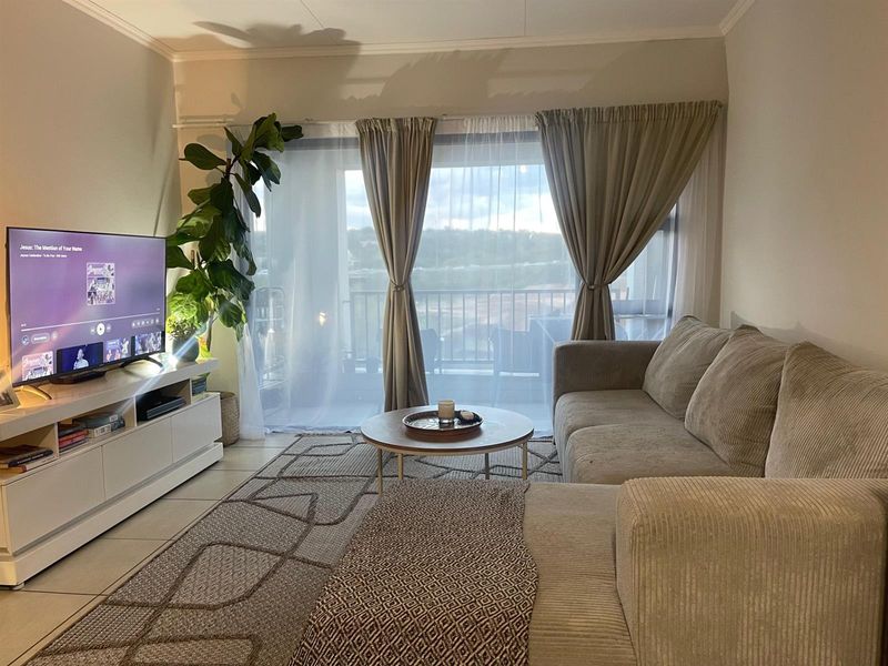 A comfortable living room featuring tiled flooring and a large sliding glass door that provides natural light and access to the balcony.