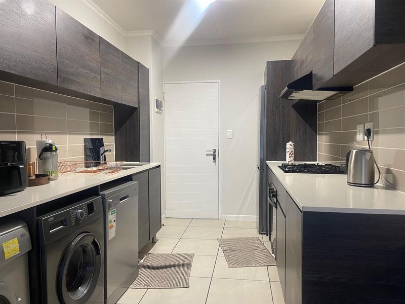 Modern galley-style kitchen featuring dark wood cabinetry, stone countertops, gas hob, extractor fan, and tiled flooring with integrated appliance space.