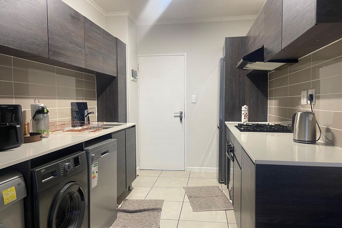 Modern galley-style kitchen featuring dark wood cabinetry, stone countertops, gas hob, extractor fan, and tiled flooring with integrated appliance space.