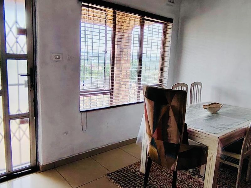 A dining area featuring tiled flooring, large windows with fitted blinds, and a security gate leading to an outdoor space.