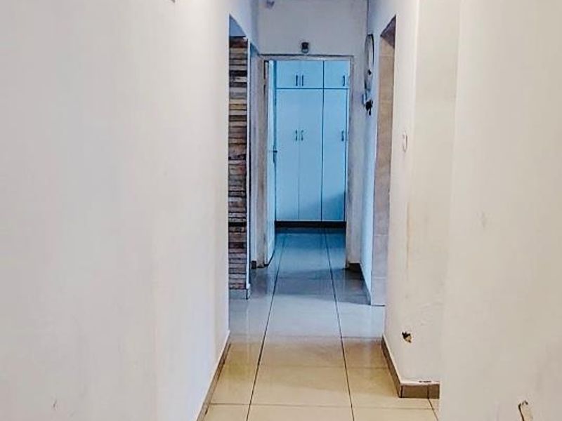 A narrow interior hallway featuring tiled flooring and access to multiple rooms, including a bedroom with built-in cupboards at the end.