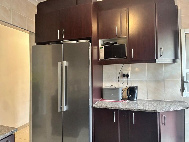 A kitchen area featuring dark wood cabinetry, granite-look countertops, and tiled splashbacks, providing functional storage and workspace.