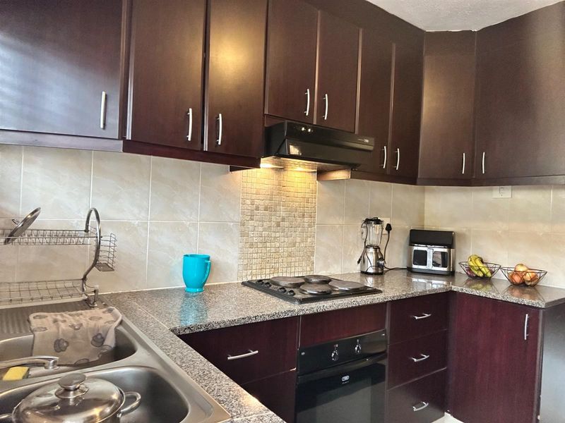 A functional kitchen featuring dark wood cabinetry, granite countertops, a built-in oven, electric hob, and a tiled backsplash.