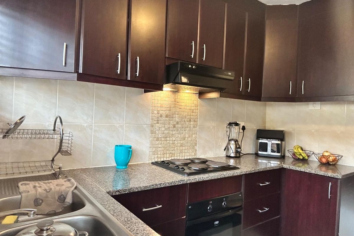 A functional kitchen featuring dark wood cabinetry, granite countertops, a built-in oven, electric hob, and a tiled backsplash.