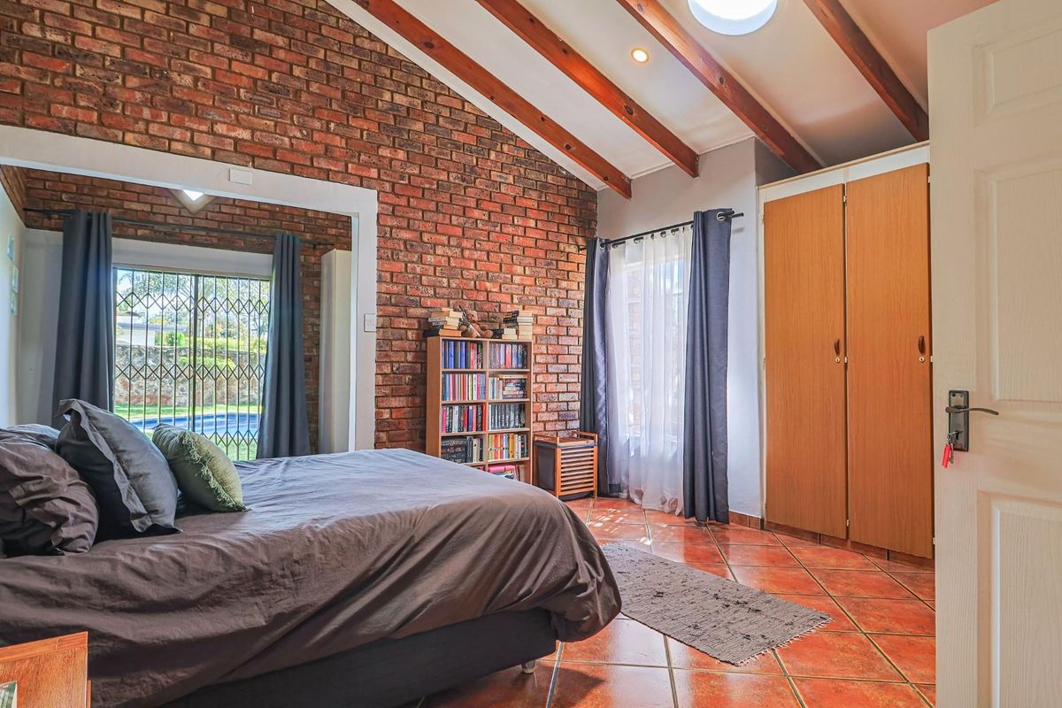 Spacious bedroom featuring a vaulted ceiling with exposed timber beams, a rustic face-brick feature wall, tiled flooring, and built-in wooden cupboards.