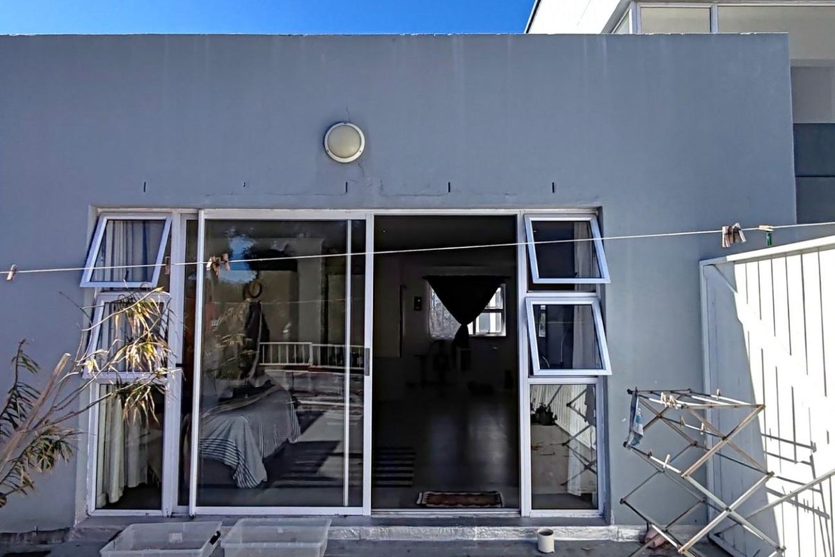 Rear view of the apartment featuring a sliding glass door entrance, exterior wall-mounted lighting, and a paved outdoor area.